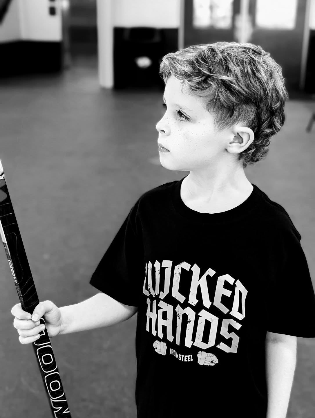 Young player holding a hockey stick in an Iron+Steel Wicked Hands tee