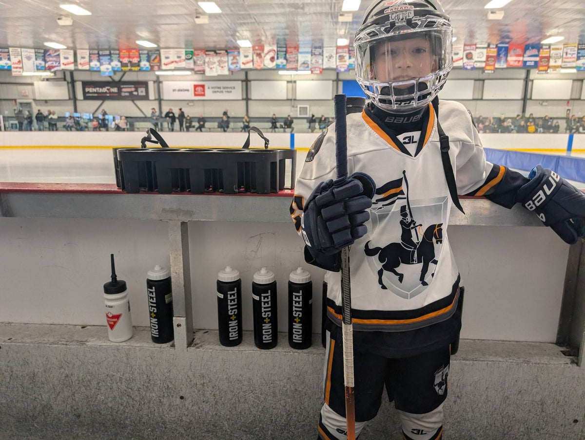 Young player in full gear on the bench beside a row of Iron+Steel water bottles
