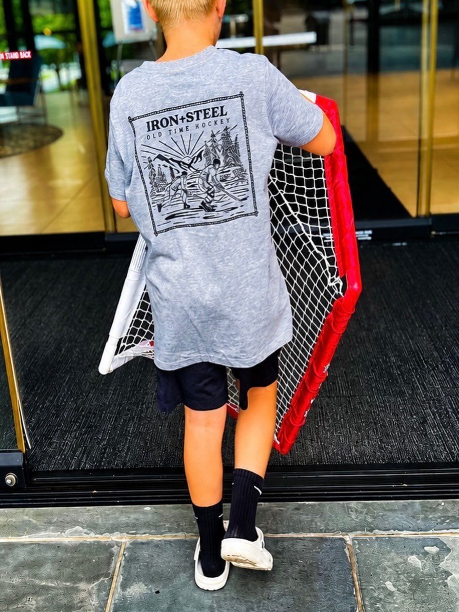 Kid carrying a street hockey net in an Iron+Steel Old Time Hockey tee