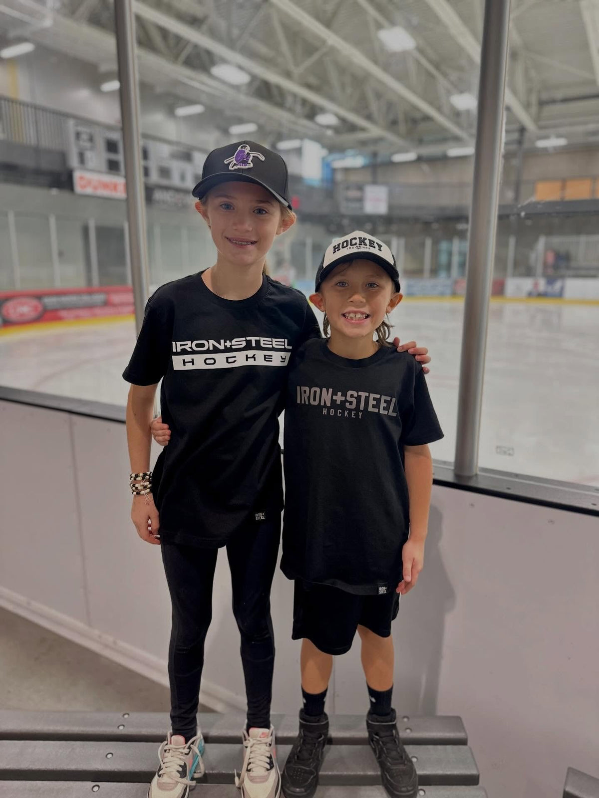 Two kids at the rink in matching black Iron+Steel Hockey tees
