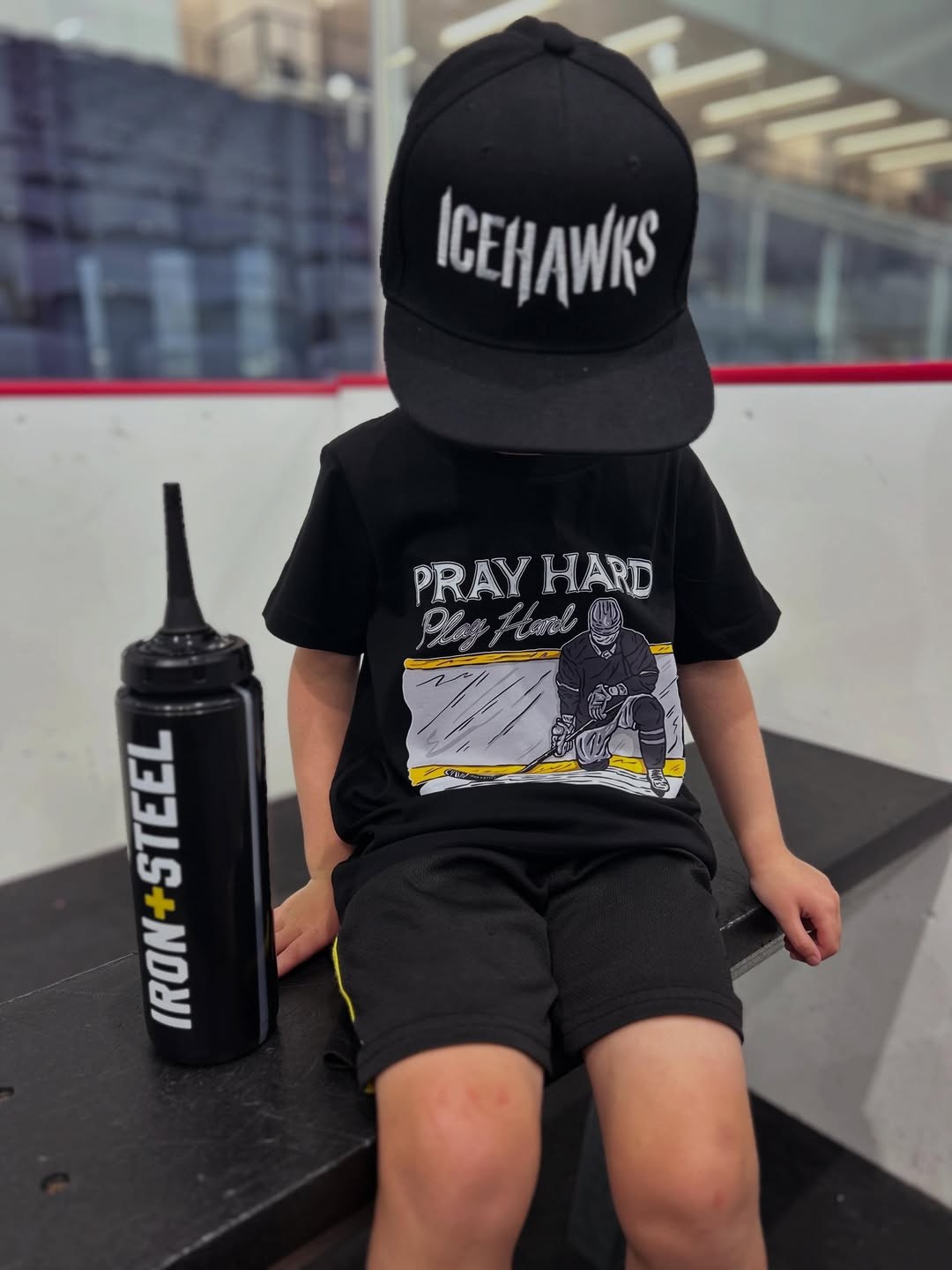 Young player on the bench in a Pray Hard Play Hard tee beside an Iron+Steel water bottle
